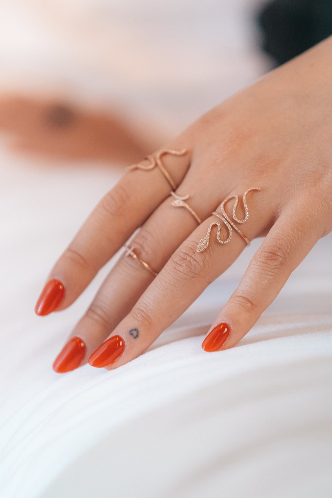 Bagues serpent pavées de diamants portées sur une main, ongles rouges